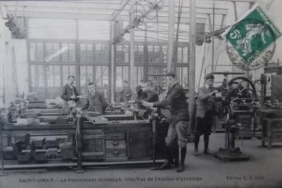 Les éléves pouvaient apprendre à se servir des machines et réaliser des travaux de mécanique générale. On peut voir les courroies qui entraînaient ces machines. Et au premier plan des éleves qui se servent d'une lime. On voit dans le fond le professeur.